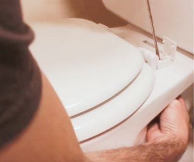 Removing the old toilet seat using a flat head screwdriver